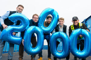 A group of people standing with blue balloons in the shape of £20,000