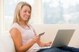 woman-in-living-room-using-laptop-and-holding-credit-card-smiling_SFDW9SjRrj