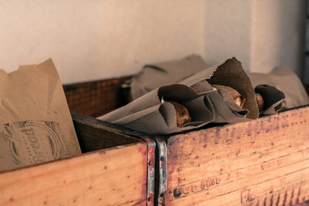Artistic photo of freshly baked bread wrapped in brown paper, placed inside a rustic wooden crate.