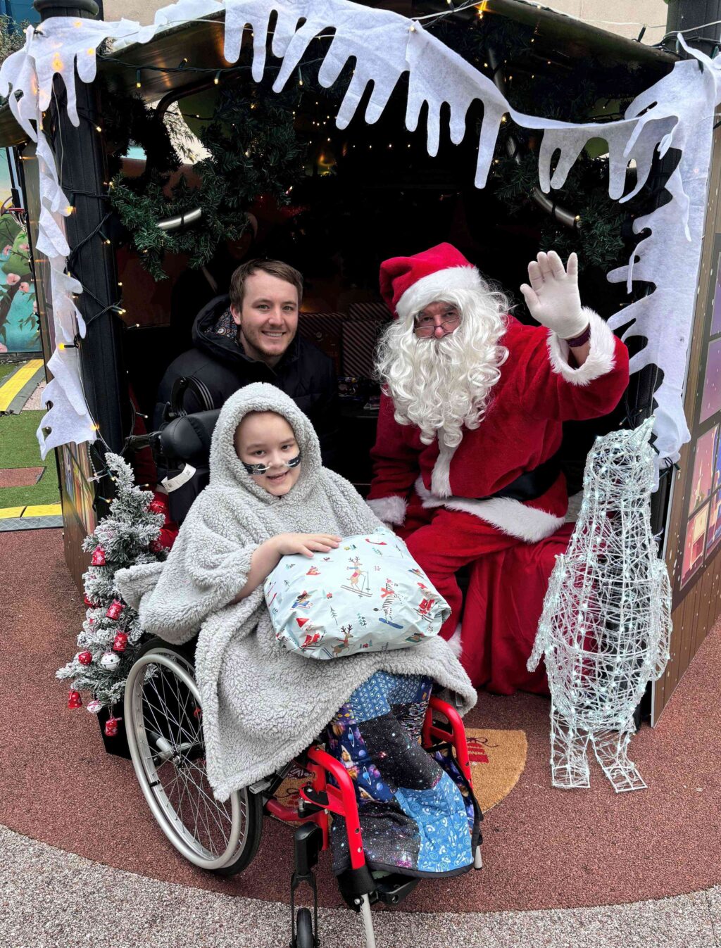 A young patient in a wheelchair visiting Santa's grotto with Santa.
