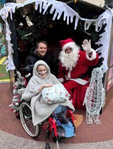 A young patient in a wheelchair visiting Santa's grotto with Santa.