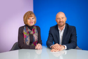 Anne Smith sat with Simon Tee at a white table with a purple and blue background.